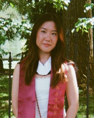 Elleen Xue in sleeveless white dress, red scarf outside tree trunk in background