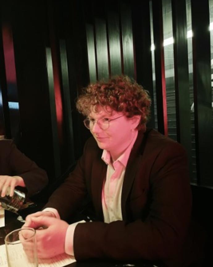 Aiden Sagerman in a suit seated at a table, hands folded