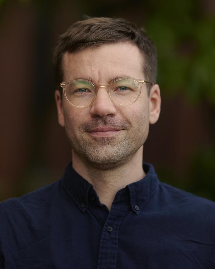 Benjamin Wilson in dark blue shirt smiling in front of wooded background